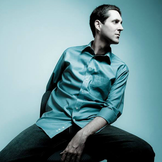 Nicolay+sitting+on+a+stool+wearing+a+satin+teal+shirt+that+matches+the+backdrop.jpg